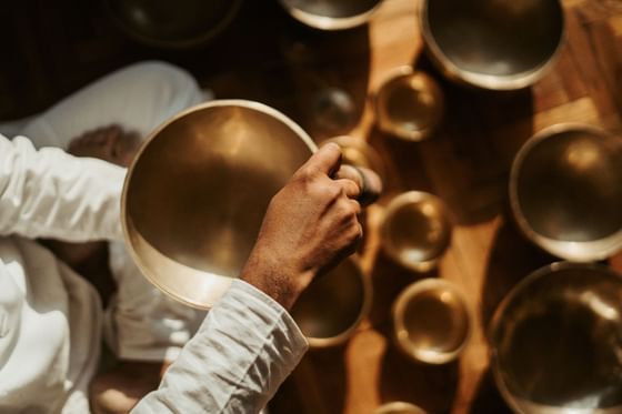 A hand holds a bronze bowl above on a wooden floor in Pancha Kosha Himalayan Spa at Dwarika's Hotel Kathmandu