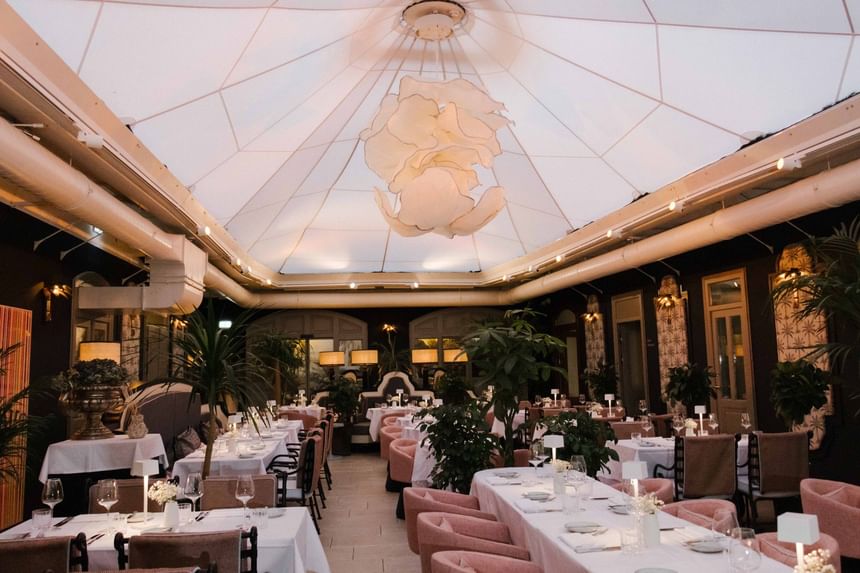 Eleganter Restaurantbereich mit rosa Samtstühlen und weißen Tischdecken unter einem beleuchteten Glasdach