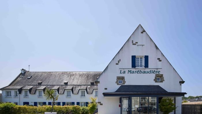 Façade de l'Hôtel La Marébaudière avec entrée et jardinières sous un ciel bleu.
