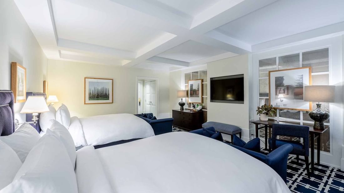 TV, work desk, and seating area by the cozy beds in Deluxe Queen Queen Room with geometric patterned carpet at El Prado Hotel