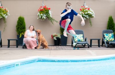 Boy jumping into an outdoor pool near a woman and dog at pet friendly hotels moncton resort property in Rodd Moncton