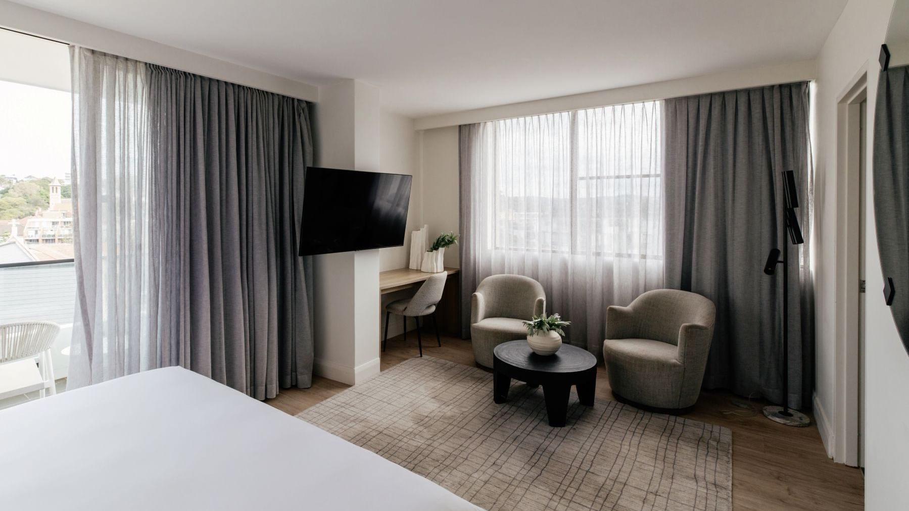 Sunset Junior Suite at Elysium Manly with grey armchairs by a black coffee table under sheer curtains near a wall-mounted TV
