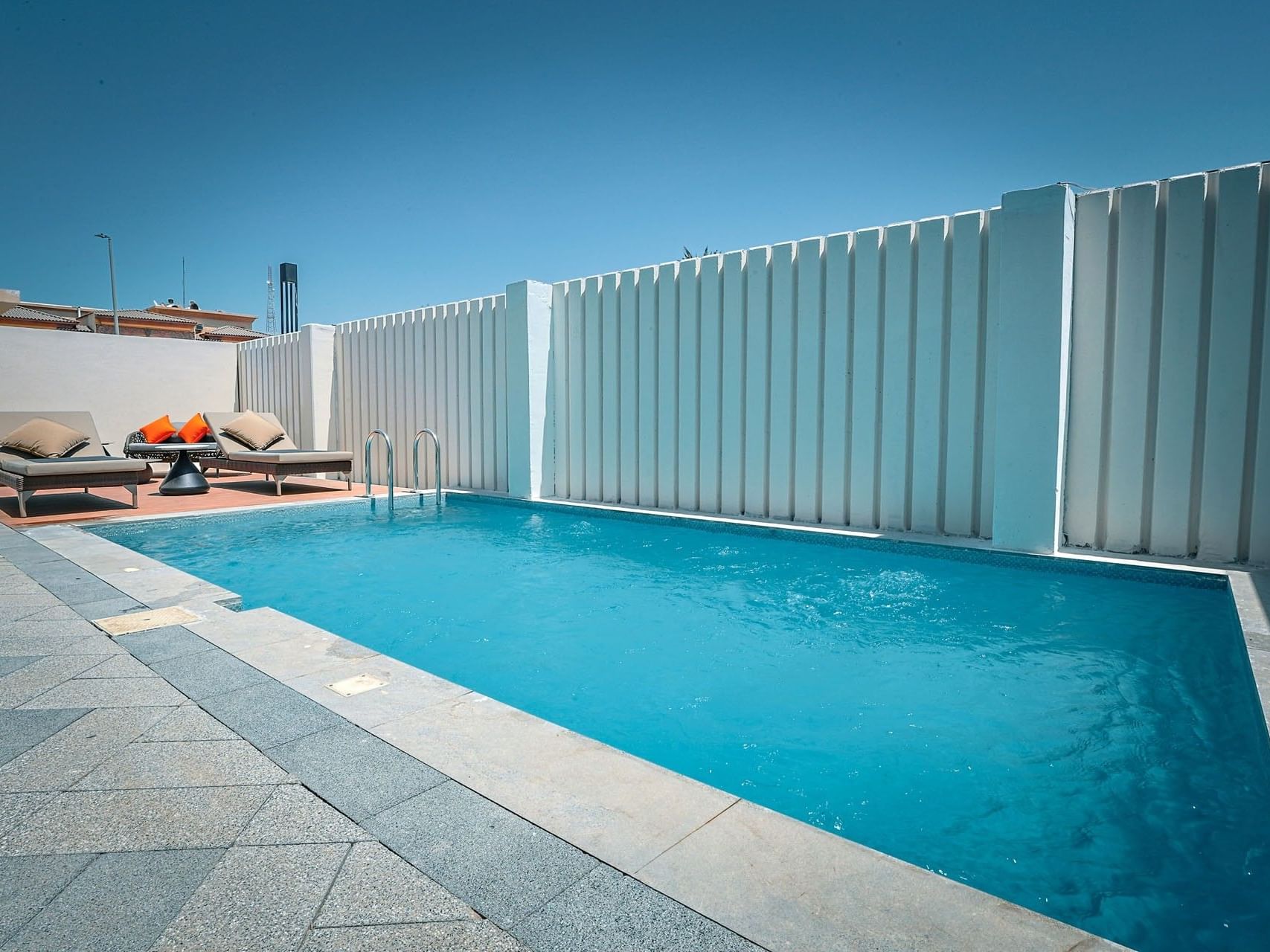 Pool with blue water and lounge chairs, set in a private outdoor area with a white slatted fence.