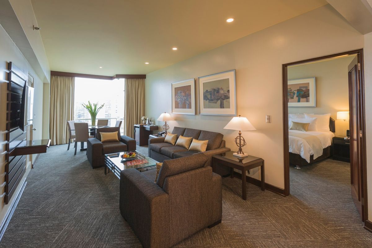Suite de hotel con sofás, mesa, sillas, cama, espejo y ventana con vista al golf.