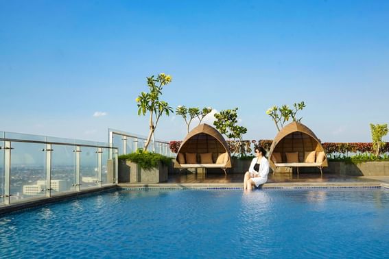 A lady sitting next to the rooftop pool at LK Pemuda Semarang Hotel & Residences