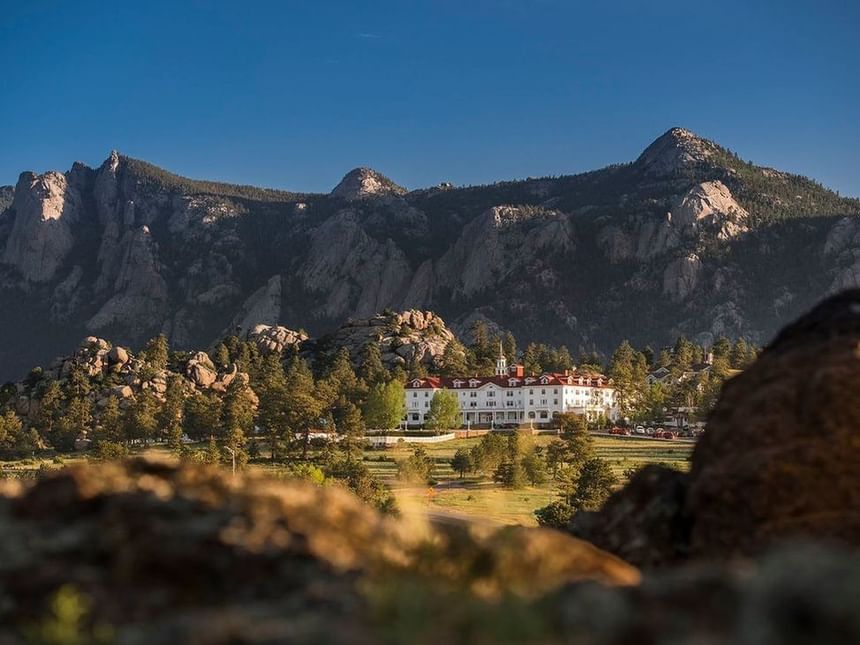 Scenic view of The Stanley Hotel featuring its white facade and red roof surrounded by lush valley and distant mountains