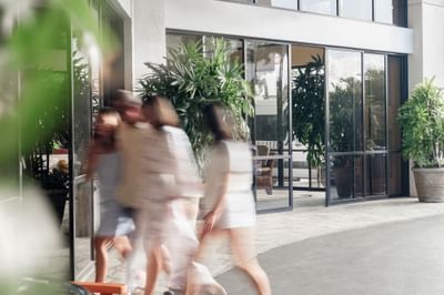 Blurry image of guests walking past the lobby entrance, with large potted plants and glass doors at the Maui Coast Hotel