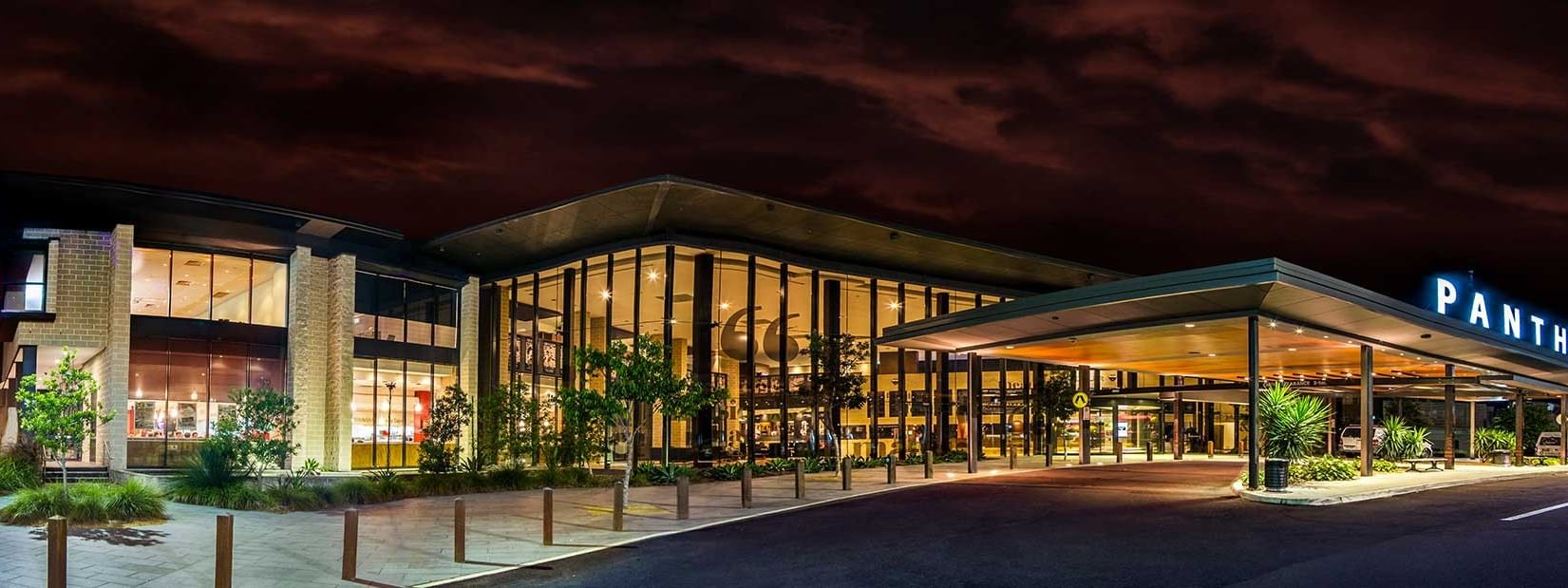 Illuminated Panthers Penrith Rugby Leagues Club at night with dark sky and driveway in front.