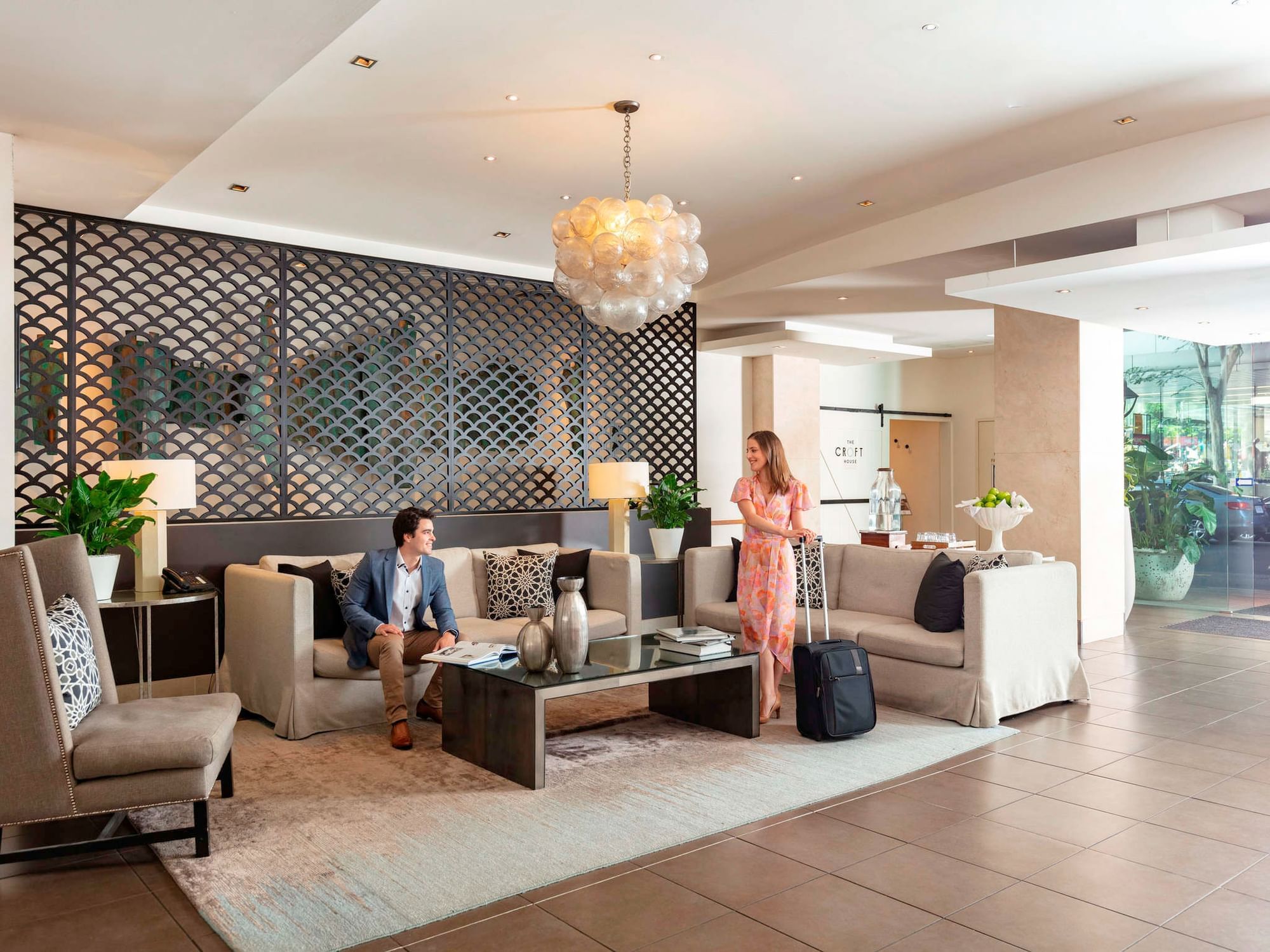 Guests relaxing in the stylish hotel lobby seating area with modern furniture and a bubble chandelier at The Sebel Brisbane