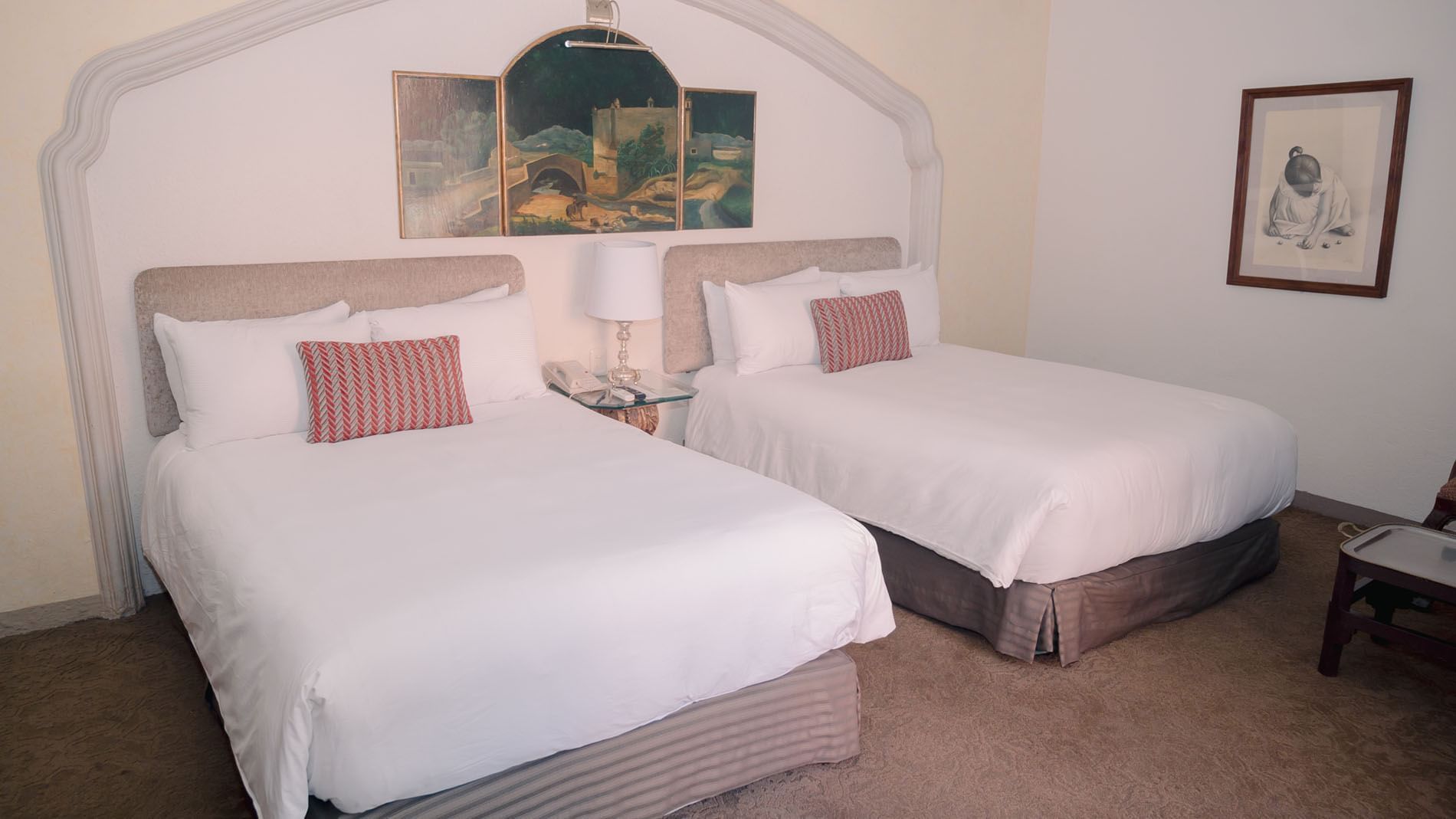 2 Double Grand Class with white sheets and red pillows, artwork on walls, and nightstand with lamp at Quinta Real Zacatecas
