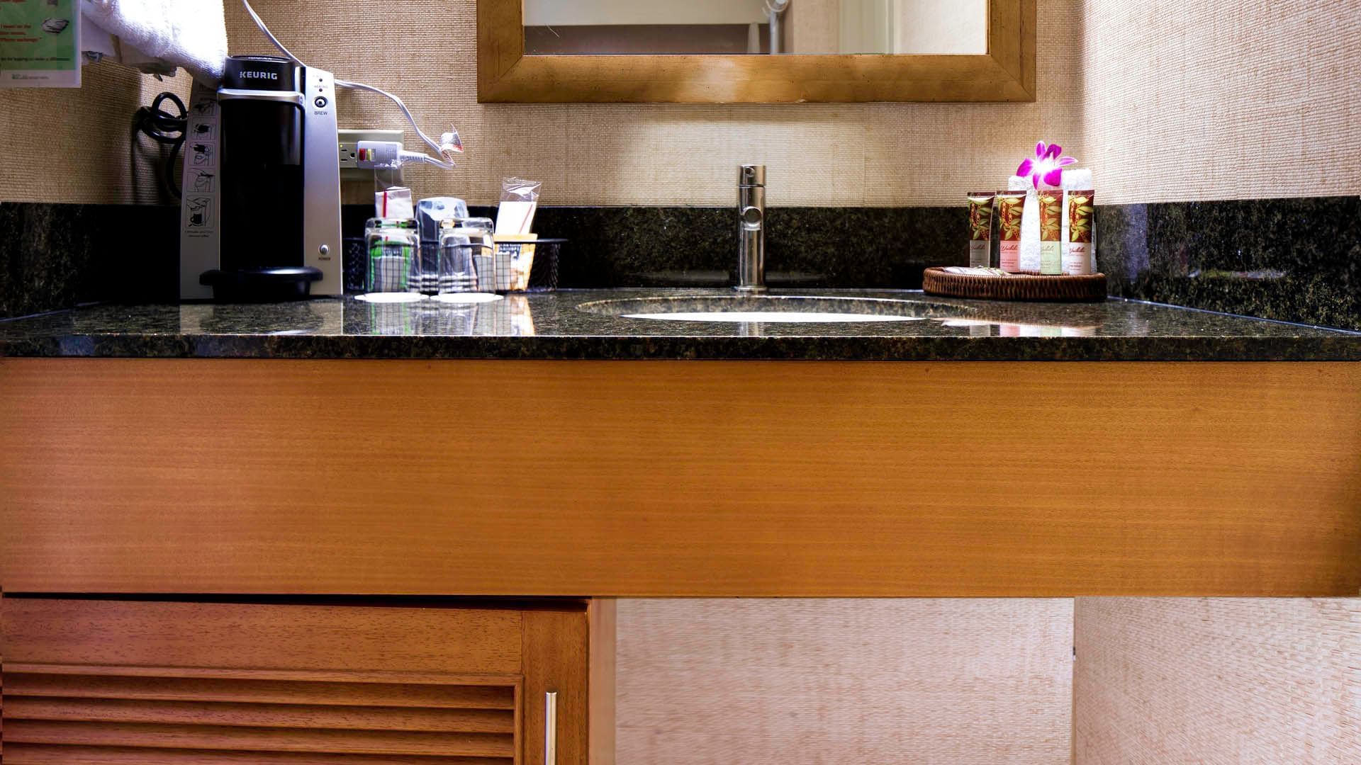 A hotel bathroom sink area with a coffee maker, sink, and amenities.