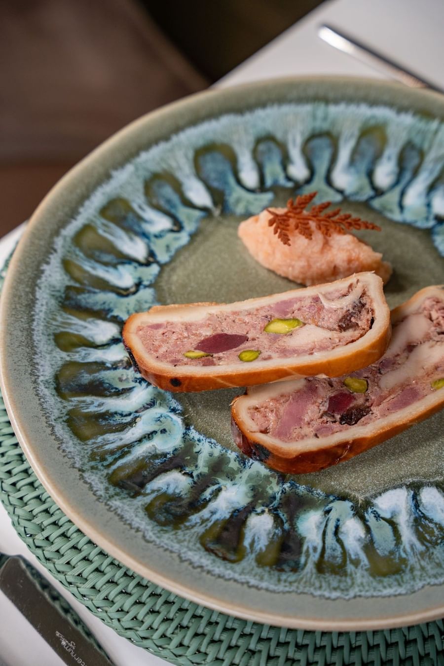 Pâté en croûte with pistachio on a textured green plate by a linen mat served in Le Céladon at Hotel Westminster Paris