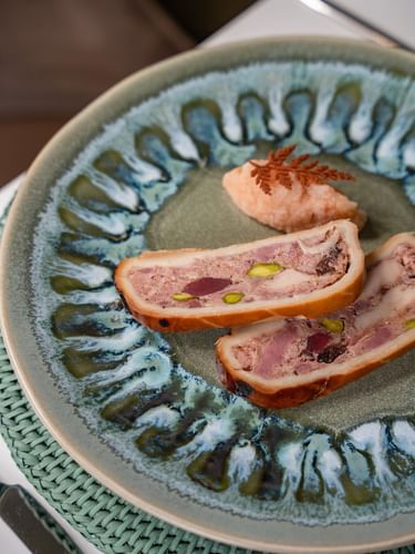Pâté en croûte with pistachio on a textured green plate by a linen mat served in Le Céladon at Hotel Westminster Paris