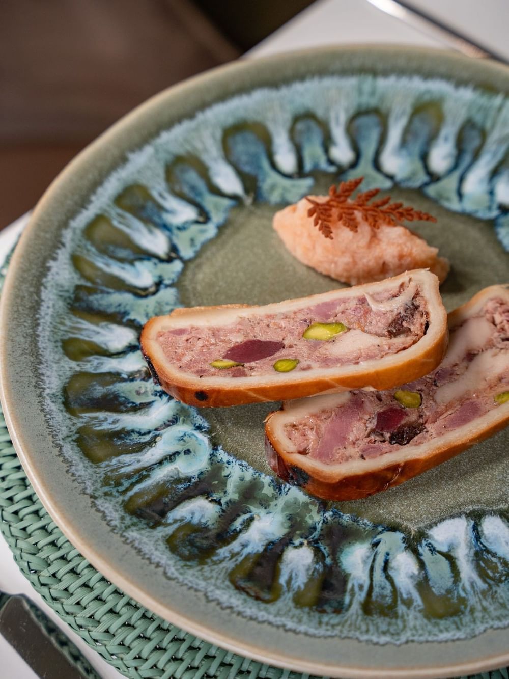 Pâté en croûte with pistachio on a textured green plate by a linen mat served in Le Céladon at Hotel Westminster Paris