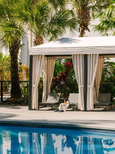 Poolside cabana with lounge chairs, refreshments, and tall palm trees on a sunny day at Kenmore Village Hotel South Beach