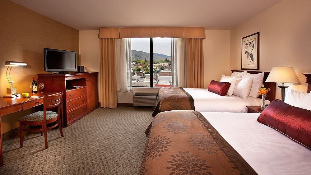 Two beds, desk and TV in hotel room with window