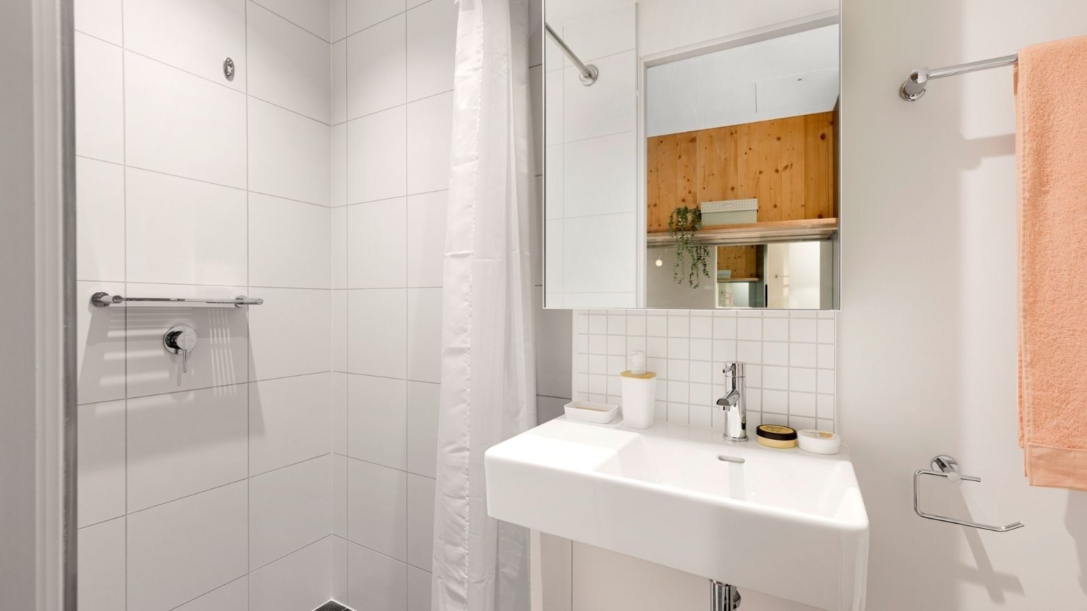 White bathroom with a sink, mirror, and shower at La Trobe University.