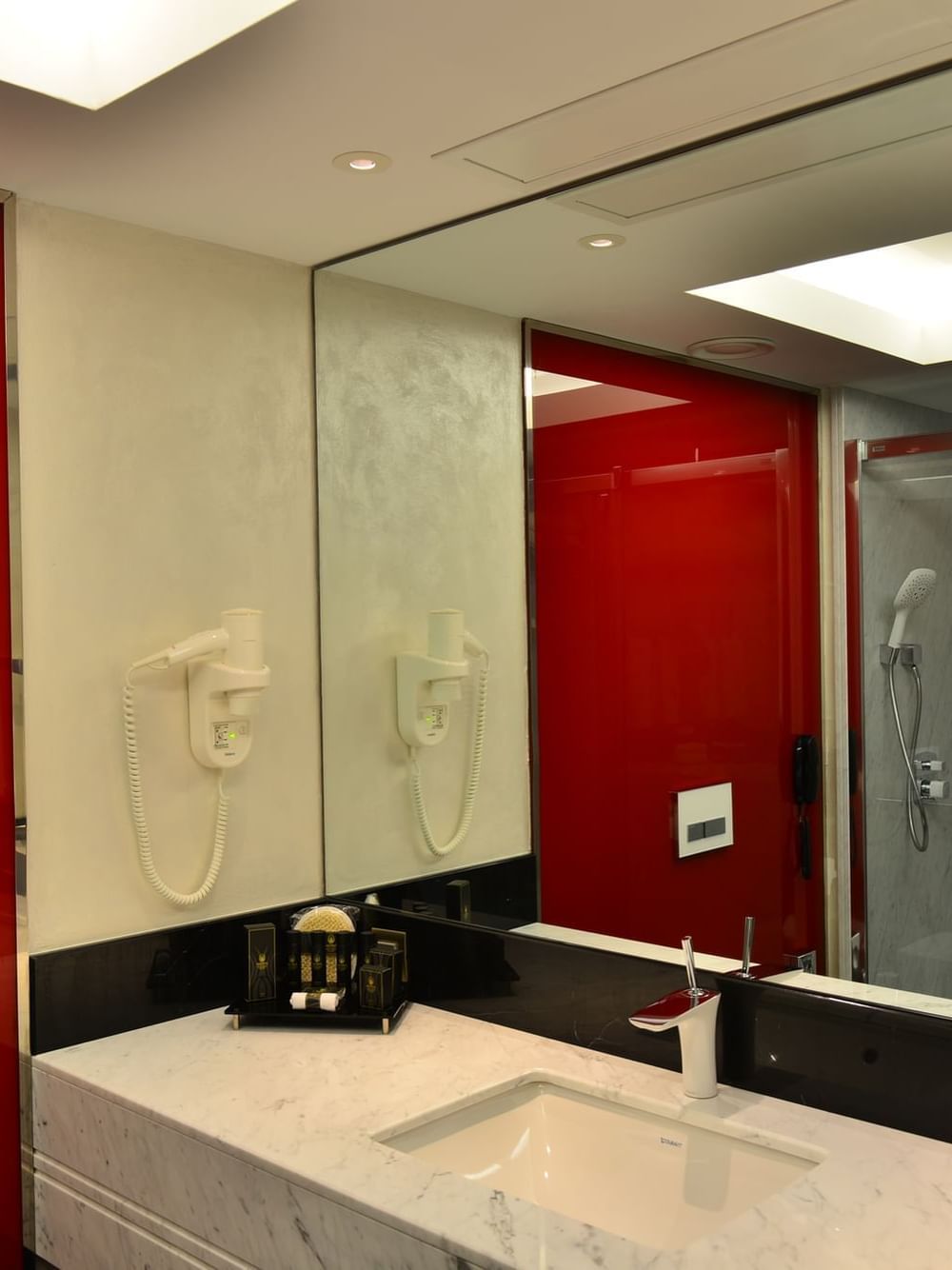 White marble sink by a red glass wall under a large mirror and bright lights in Deluxe Rooms at Warwick Ankara