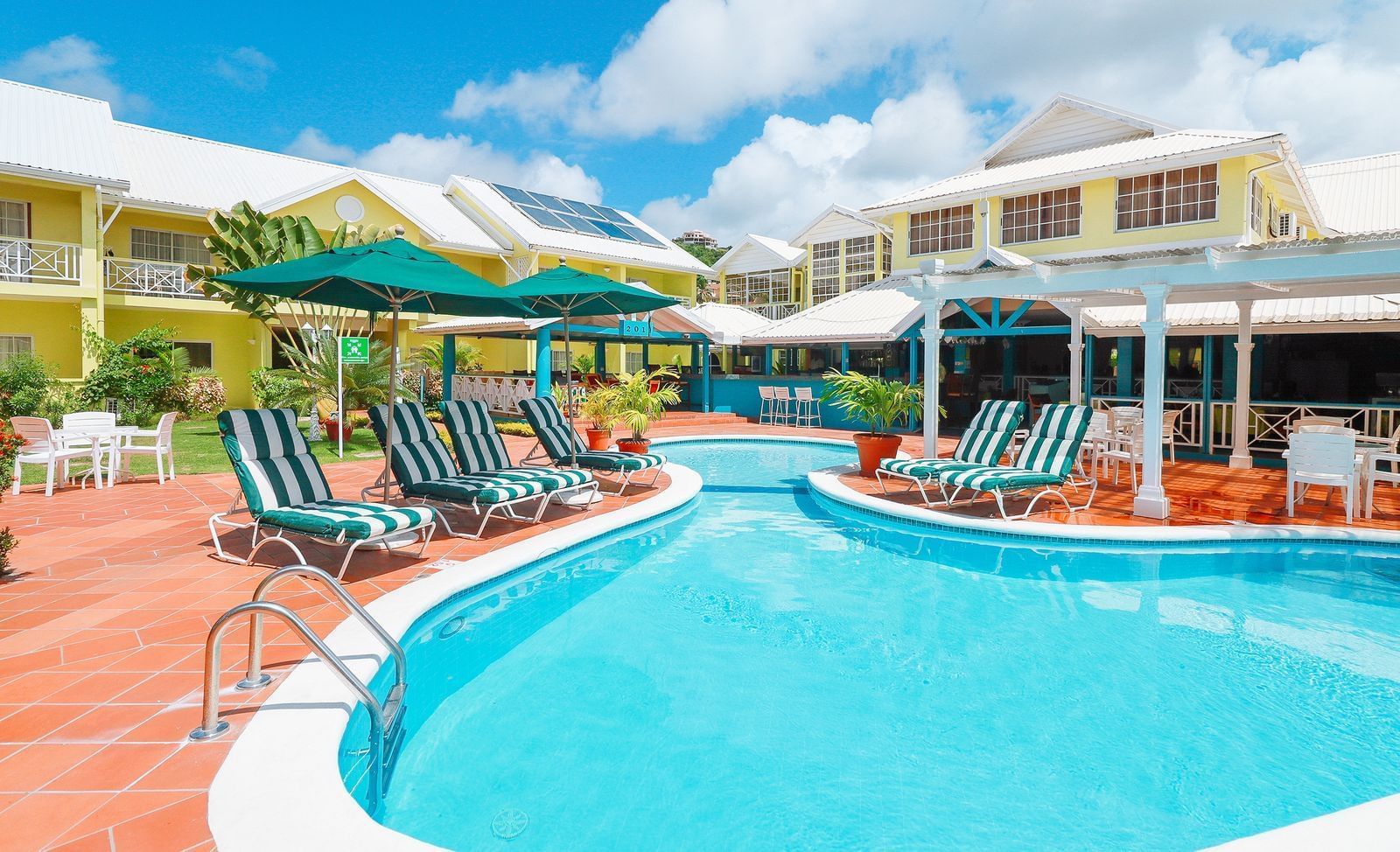 Vibrant pool area with striped lounge chairs, green umbrellas, and colorful tropical plants at Bay Gardens Hotel