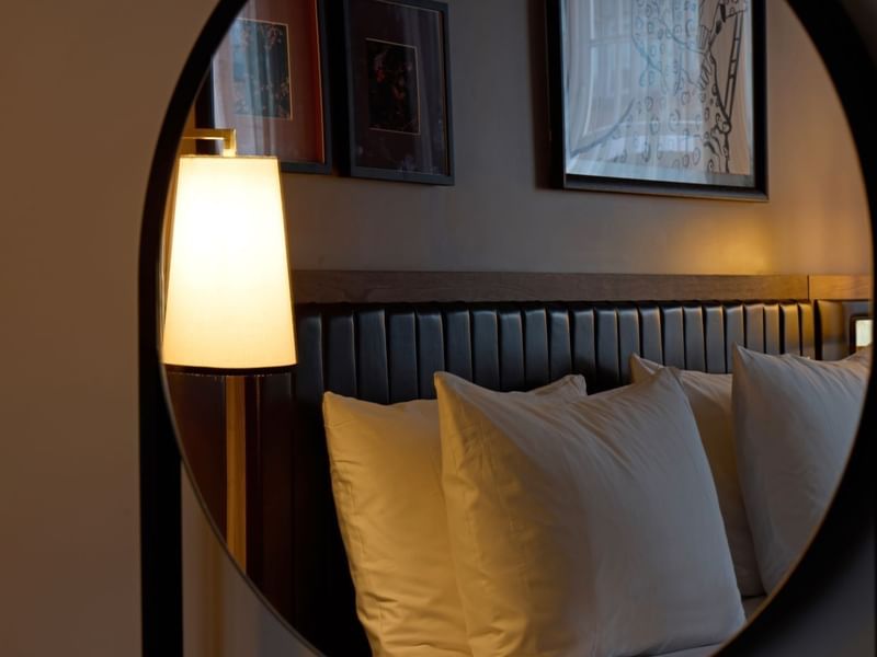 A cozy bed with white pillows and a lit lamp, reflection of a Collection Superior Bedroom in the mirror at The May Fair Hotel, London..