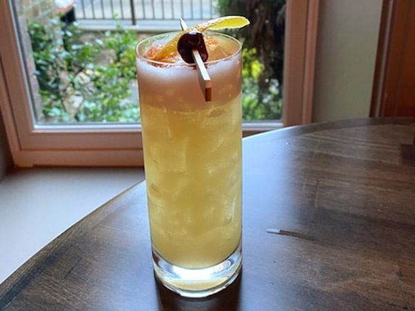 Tall cocktail with a frothy top, garnished with a cherry and citrus served in Apropos Restaurant & Bar at The Abbey Inn & Spa
