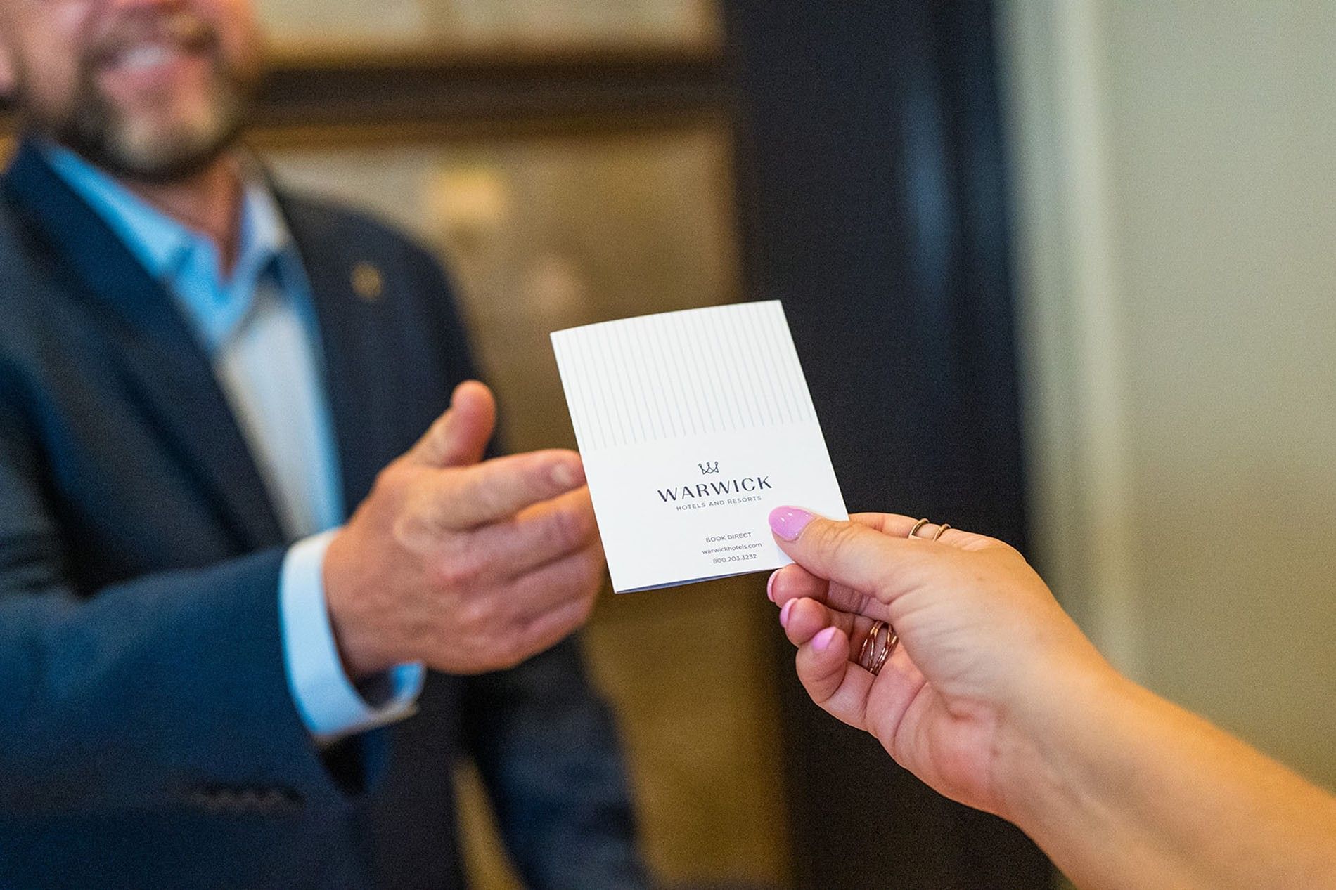 Guest taking a white service card from a staff member by a dark doorway at at Warwick Melrose Dallas