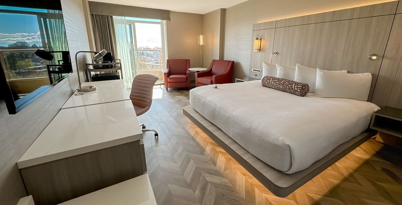 Hotel guestroom with king bed, TV, two sofas, work desk, chair, and a view of the city