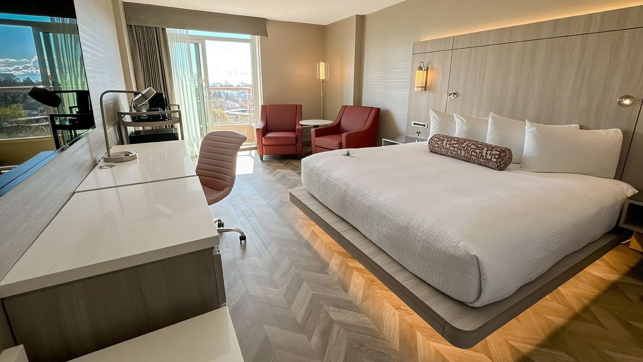 Hotel guestroom with king bed, sofas, work desk, TV, chair, and window.