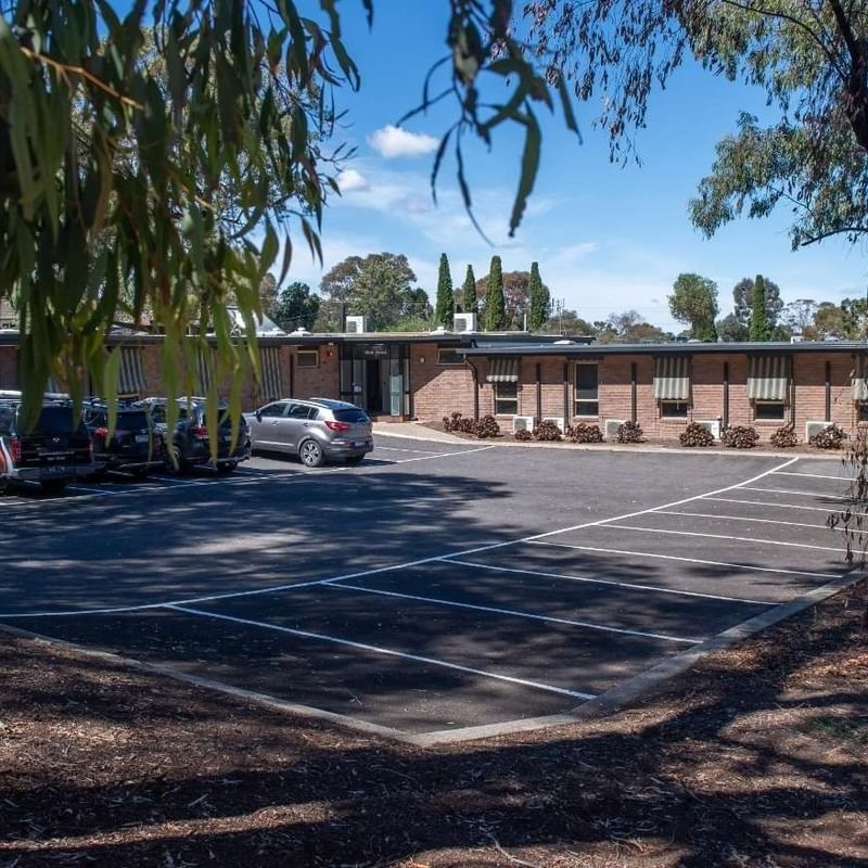 Parking lot with several cars parked in front of the La Trobe University - Orde House building.