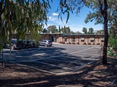 Parking lot with several cars parked in front of the La Trobe University - Orde House building.