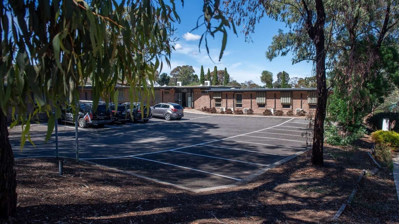 Parking lot with several cars parked in front of the La Trobe University - Orde House building.