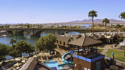 Waterfront resort with pool, water slide, and bridge spanning the river with mountains in the distance