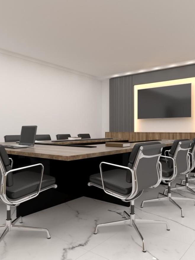 Black leather chairs by a wooden table under a large wall-mounted monitor in Orchid 1 at Cantonal Hotel by Warwick Riyadh