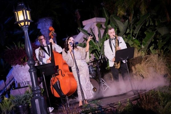 A singer, bassist, and saxophonist in formalwear perform onstage during Jollywood Nights. 