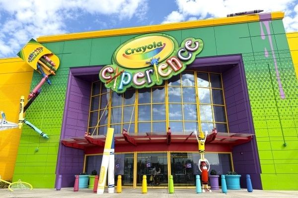 The colorful exterior of Crayola Experience at the Florida Mall, with statues of crayon characters and crayons spilling out of a box from the side of the building.