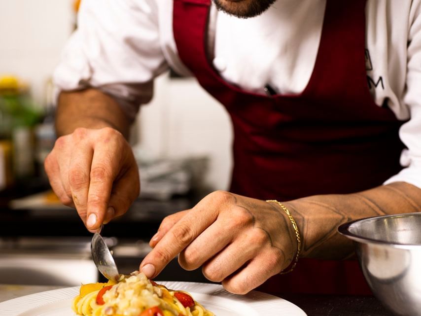 A chef garnishing served creamy pasta plate at EMME Restaurant