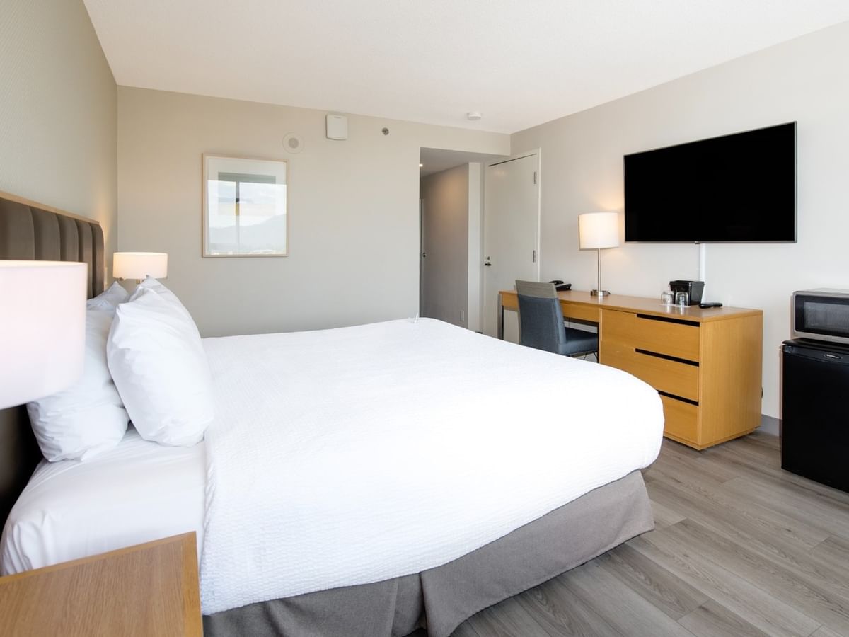 Hotel room with large king bed, work desk, TV, mini-fridge, and wooden floors.
