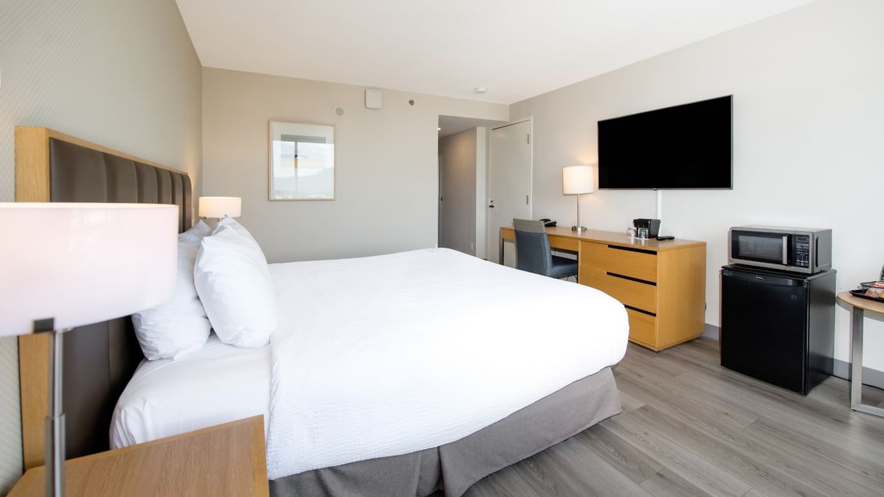 Hotel room with large king bed, work desk, TV, mini-fridge, and wooden floors.