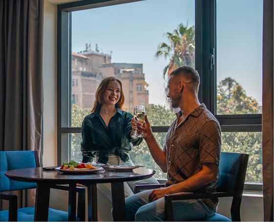 Casal brindando com vinho branco em quarto com vista para palmeiras e edifícios urbanos no Cumbres Lastarria