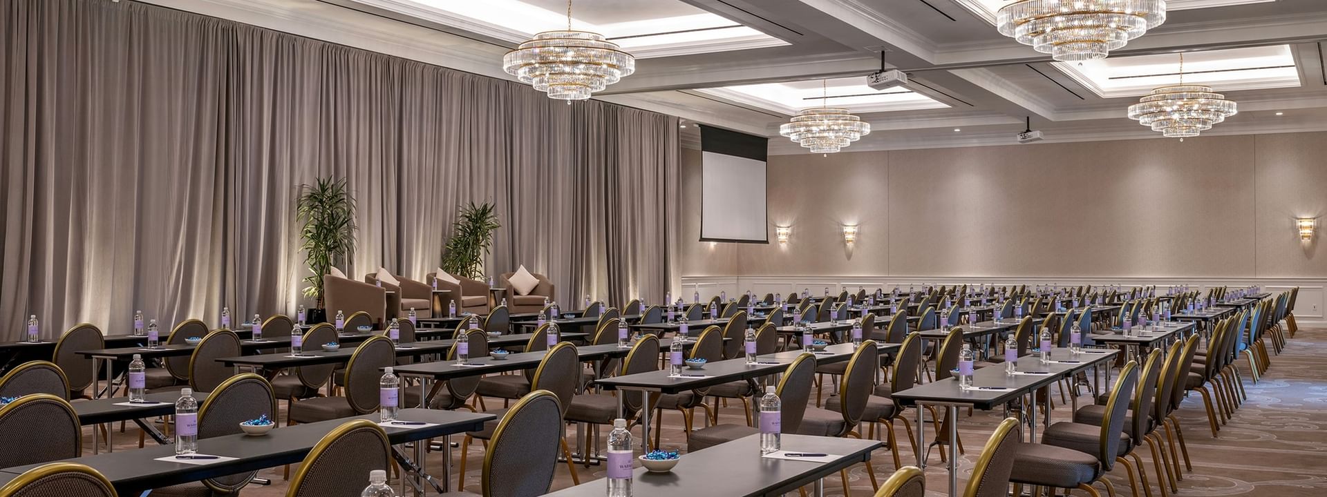 Classroom tables by water bottles under crystal chandeliers in Turtle Creek Ballroom C at Warwick Melrose Dallas