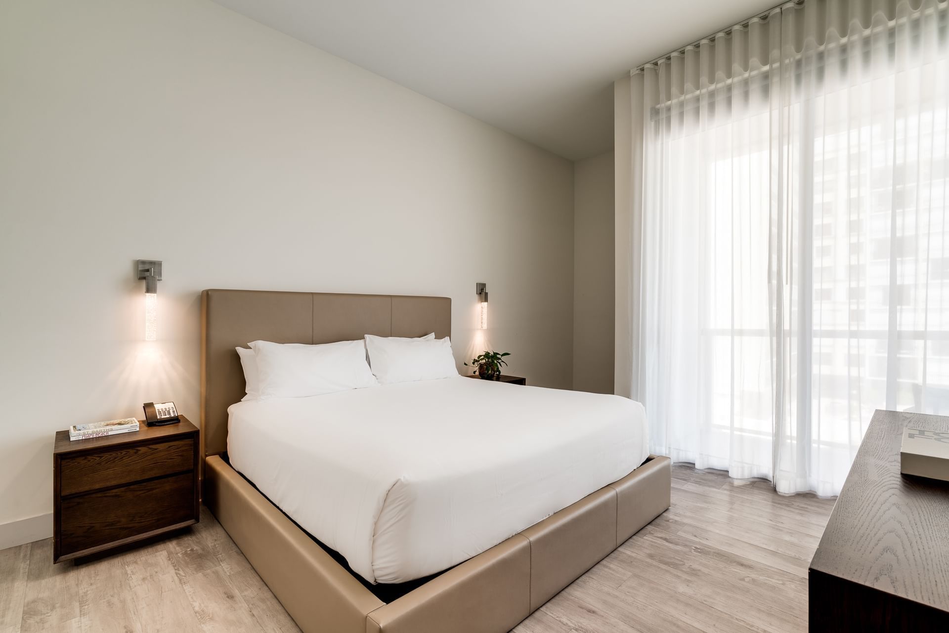 A wide view of a hotel room with a bed, nightstand, and window
