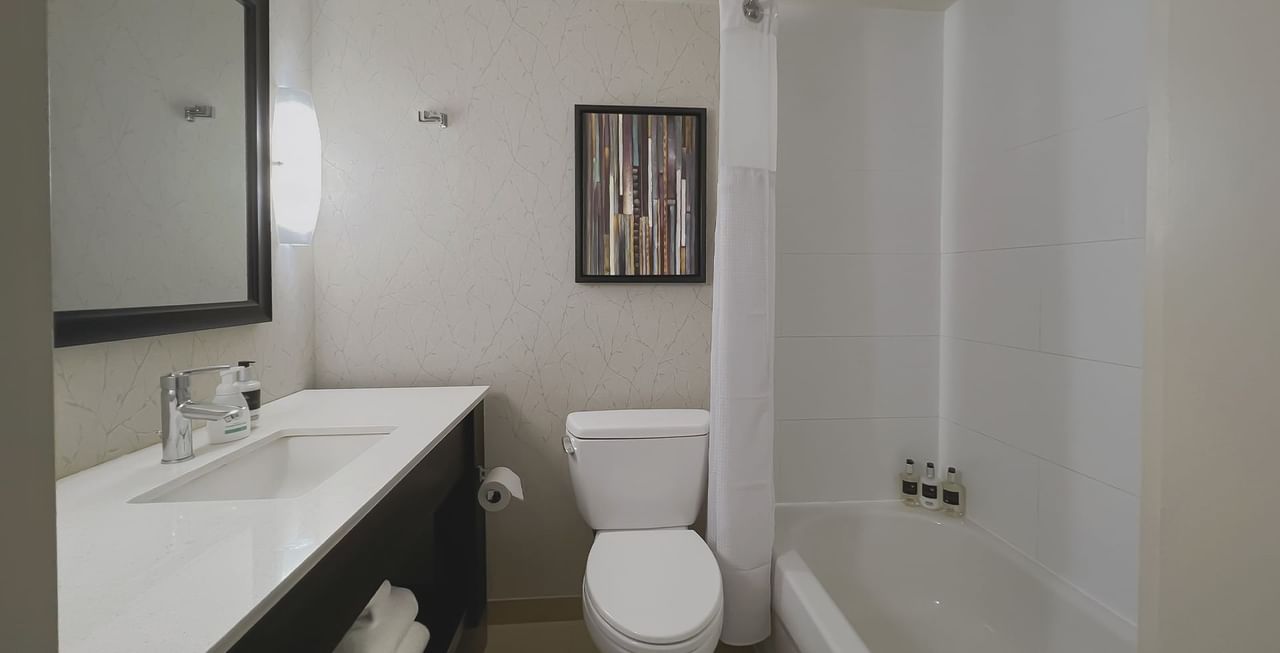 Hotel bathroom with bath tub, toilet, sink, soap, mirror, and towels
