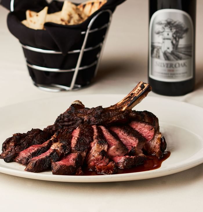 Plate of grilled steak with sauce, basket of bread, and a bottle of wine served at the Hotel Arista.