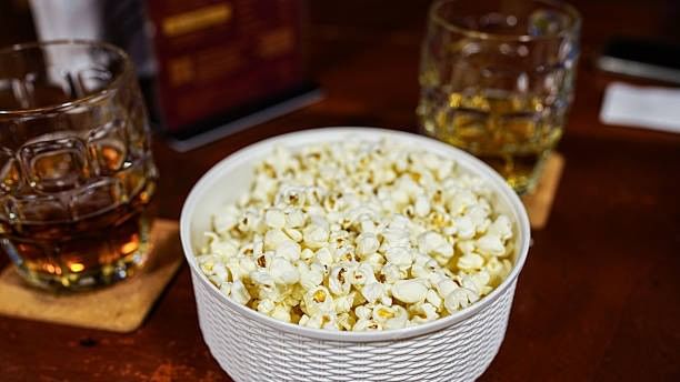 Bowl of popcorn with glasses of beverages on wooden table for Kid Vacation Kick Off event