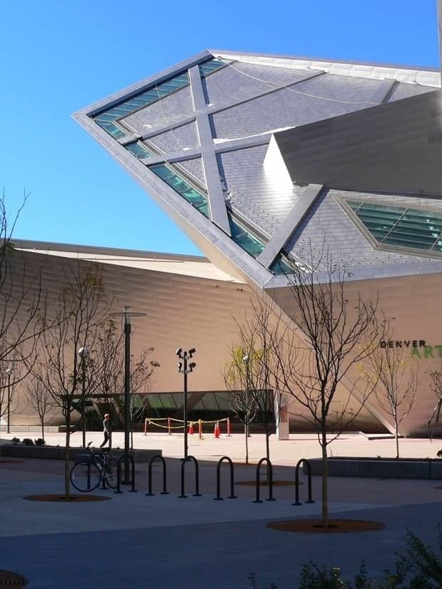 Denver Art Museum exterior with geometric panels by bare trees under a blue sky near Warwick Denver