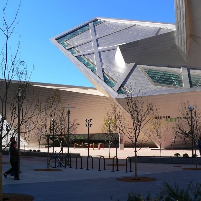 Denver Art Museum exterior with geometric panels by bare trees under a blue sky near Warwick Denver