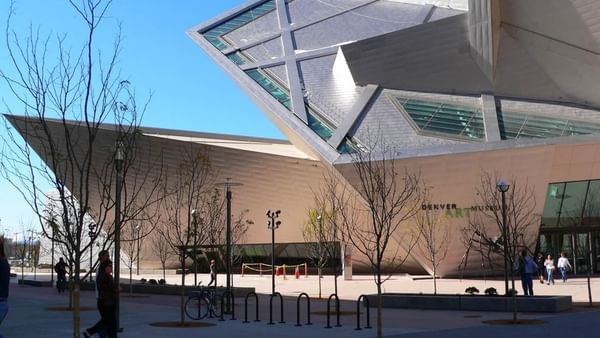 Denver Art Museum exterior with geometric panels by bare trees under a blue sky near Warwick Denver