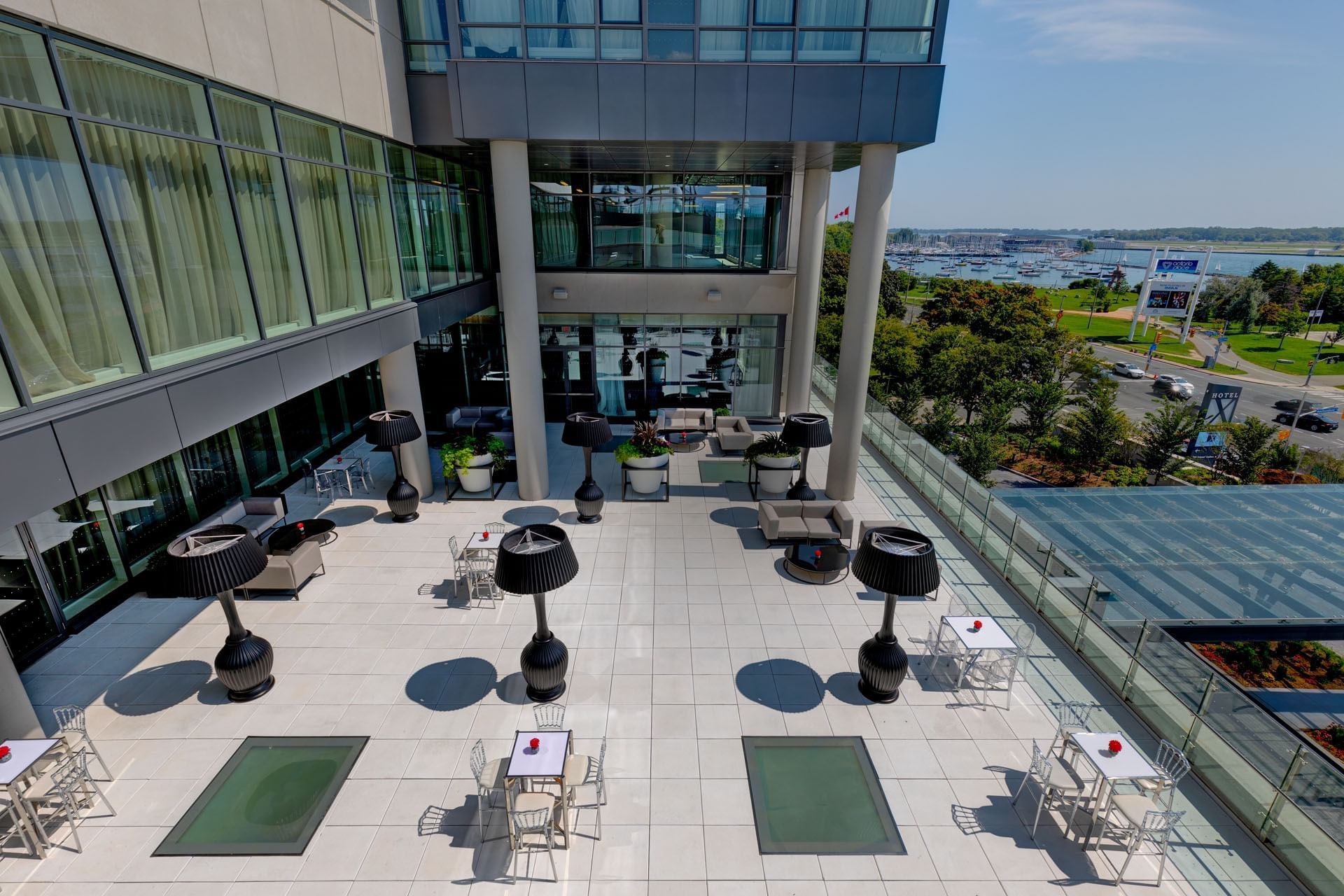 High angle view of Marina terrace with black floor lamps and small tables beside glass canopy at Hotel X Toronto