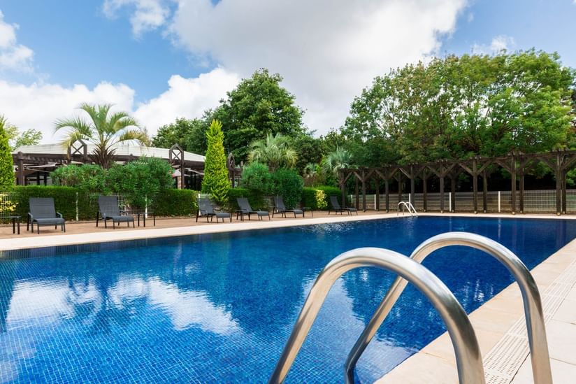 Swimming pool with loungers & trees around at Oceania Hotels