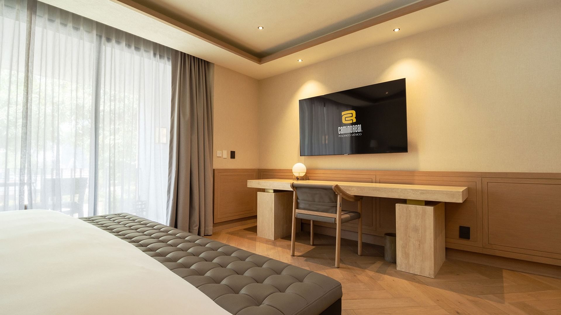 Habitación de hotel moderna con cama, escritorio, silla, televisión y ventana con cortinas.